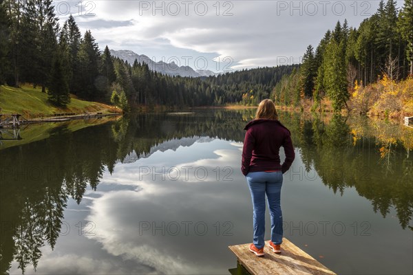 Female hiker stands on a footbridge and looks across the lake