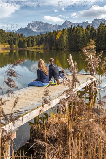 Two young women sitting at a jetty having a snack