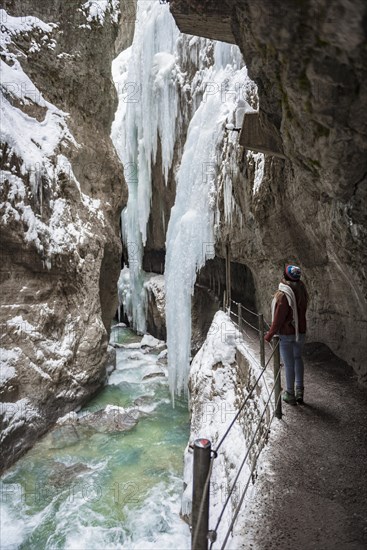 Young woman in the icy Partnachklamm with icicles and snow in winter