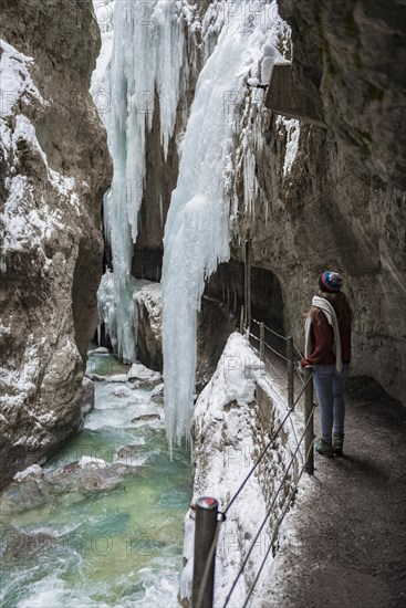 Young woman in the icy Partnachklamm with icicles and snow in winter