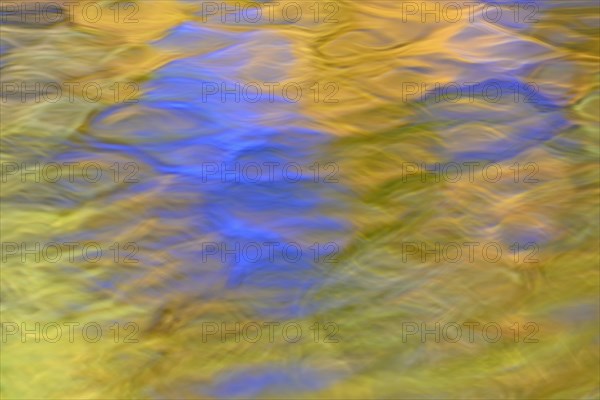 Reflection of treetops with autumn leaves on a wavy water surface