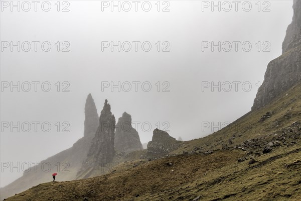Rock Old Man of Storr with tourist with red umbrella in fog