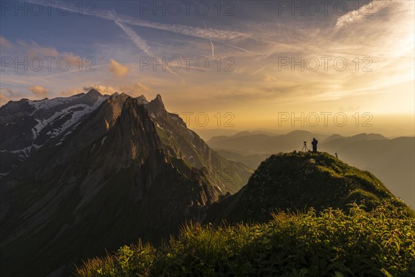 Photographer on grassy ridge at sunset with Santis peak in the background