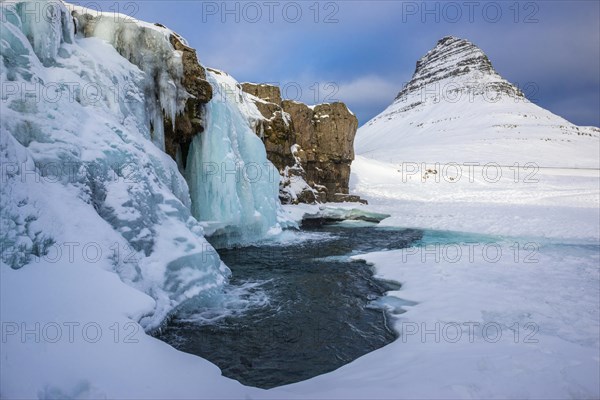 Frozen waterfall Kirkjufellsfoss and the mountain Kirkjufell with snow