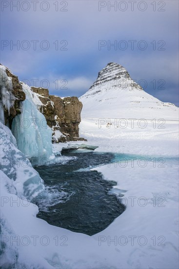 Frozen waterfall Kirkjufellsfoss and the mountain Kirkjufell with snow