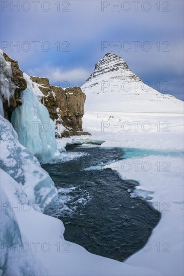 Frozen waterfall Kirkjufellsfoss and the mountain Kirkjufell with snow