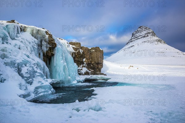 Frozen waterfall Kirkjufellsfoss and the mountain Kirkjufell with snow