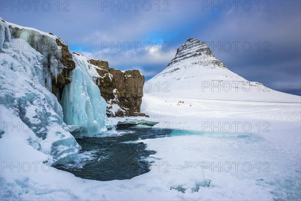 Frozen waterfall Kirkjufellsfoss and the mountain Kirkjufell with snow