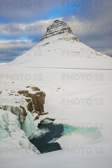 Frozen waterfall Kirkjufellsfoss and the mountain Kirkjufell with snow