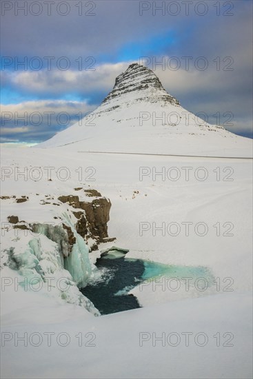 Frozen waterfall Kirkjufellsfoss and the mountain Kirkjufell with snow