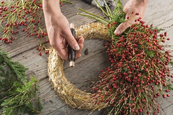 Autumn wreath on wood panel is bounded by hands with binding tool