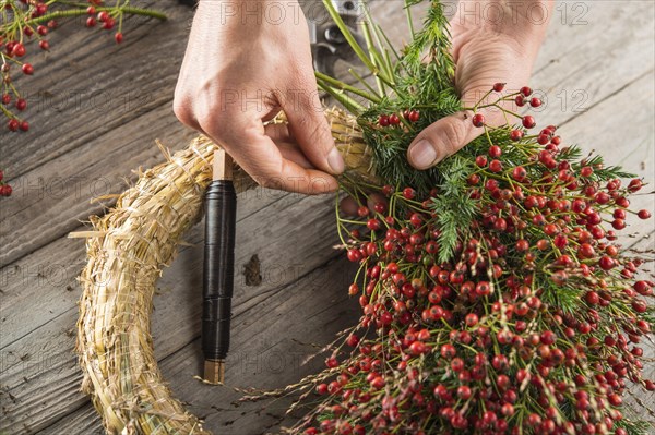 Autumn wreath on wood panel is bounded by hands with binding tool