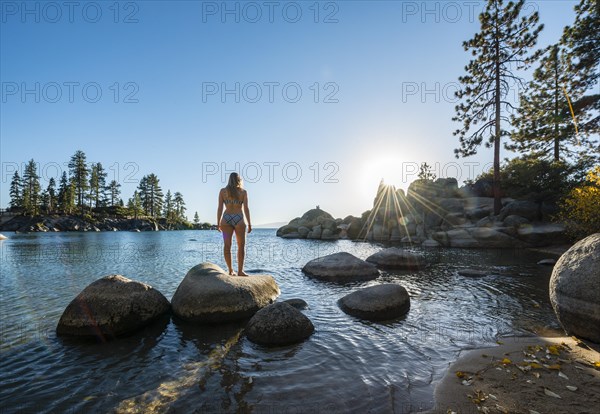 Young woman in bikini standing on a round stone in the water