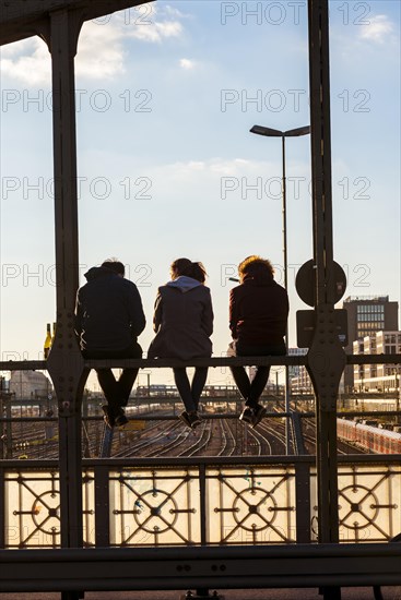 Three youths sitting on the balustrade of the Hackerbrucke bridge over the railway tracks looking into the distance