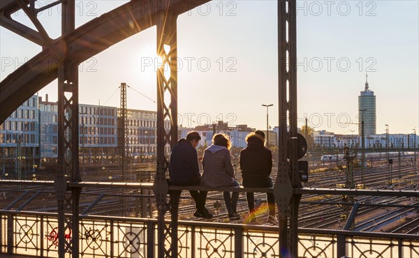 Three youths sitting on the balustrade of the Hackerbrucke bridge over the railway tracks looking into the distance