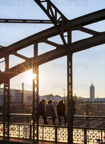 Three youths sitting on the balustrade of the Hackerbrucke bridge over the railway tracks looking into the distance