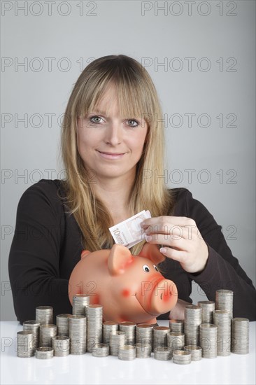 Young woman putting a ten euro bill in a piggy bank