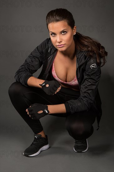 Young woman with dark hair tied together poses in a sporty outfit