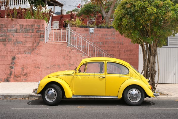 Yellow VW Beetle stands in front of red wall on the Canary Island La Palma