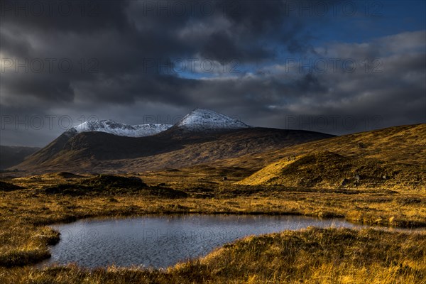 Small lake in the foreground snow-covered mountain peaks of Meall aÂ´Bhuiridh and Clach Leathad in the background and dramatic clouds