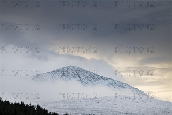 Snow-covered mountain top with clouds in snow-covered landscape