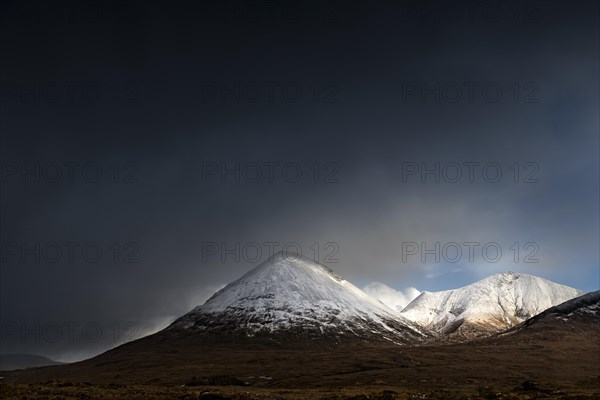 Moor landscape with snow-covered peaks of the Cullins Mountains in front of dramatic clouds in Highland Landscape