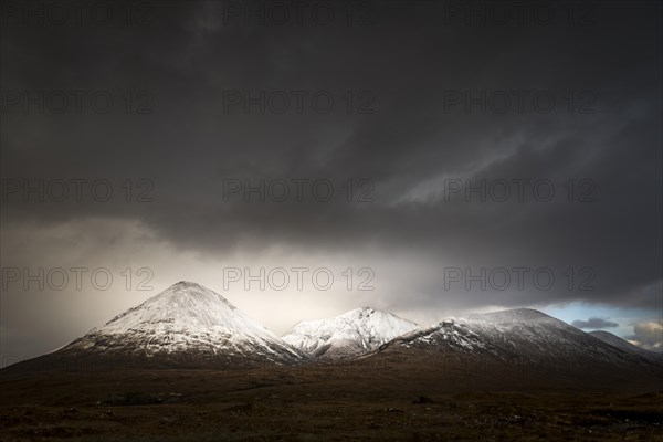 Moor landscape with snow-covered peaks of the Cullins Mountains in front of dramatic clouds in Highland Landscape