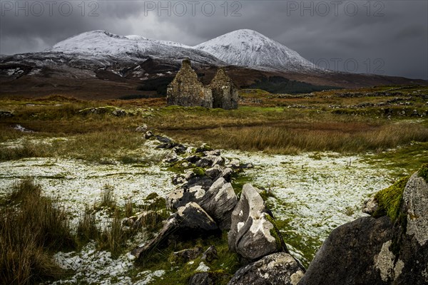 Rock row with white caps and house ruin in Highland scenery with snowy Cullin mountains in the background
