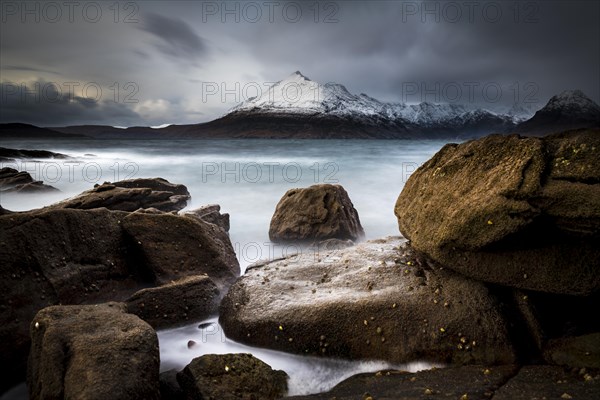 Big rocks in the water of the North Sea with snow-covered Cullin mountains in the background