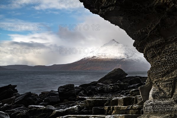 Big rocks in the water of the North Sea with snow-covered Cullin mountains in the background