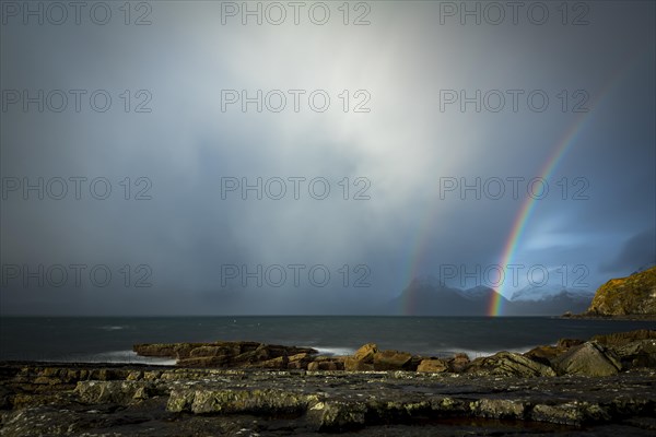 Big rocks in the water of the North Sea with snowy Cullin mountains and rainbow in the background