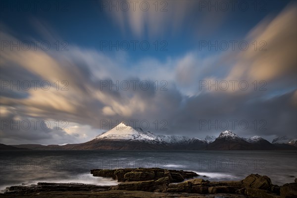 Big rocks in the water of the North Sea with snow-covered Cullin mountains in the background