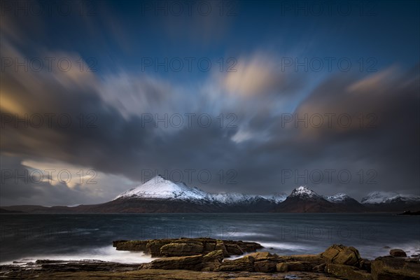 Big rocks in the water of the North Sea with snow-covered Cullin mountains in the background