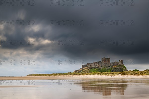 Flat sandy coast with Bamburgh Castle and reflection in the water with dark clouds