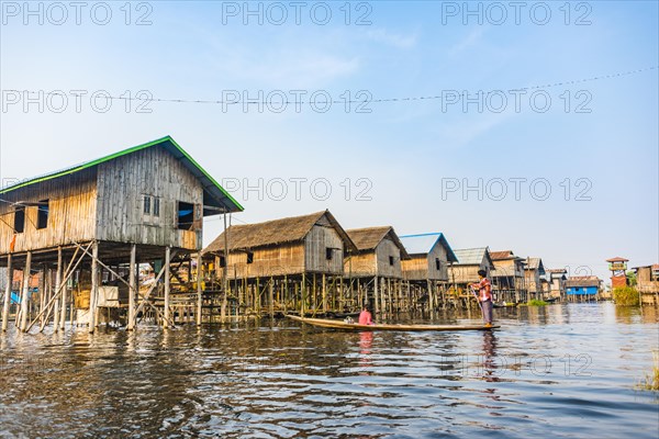 Wooden boat with locals in front of traditional stilt houses on Inle Lake