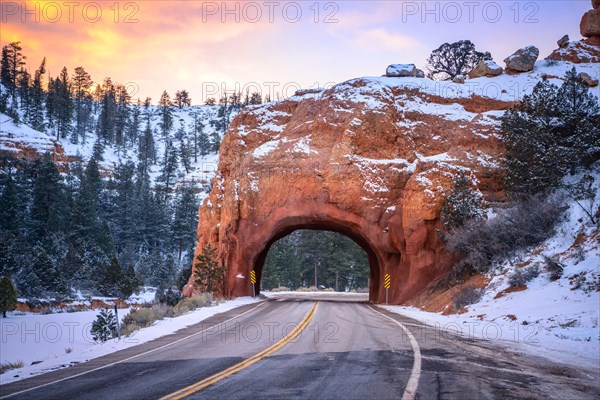 Road with tunnel through red rock arch in snow