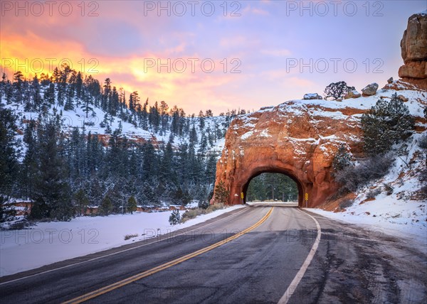 Road with tunnel through red rock arch in snow