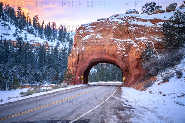 Road with tunnel through red rock arch in snow