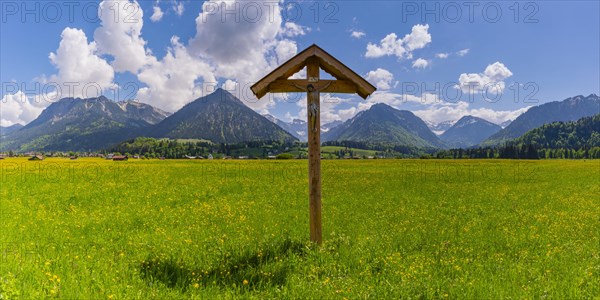 Field cross with Christ figure in front of mountain landscape