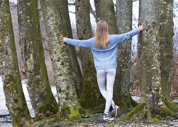 Young girl from behind with long blond hair leaning on trees