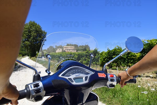 Woman holding handlebars of Vespa Primavera scooter traveling in the Sant'Amico wine country