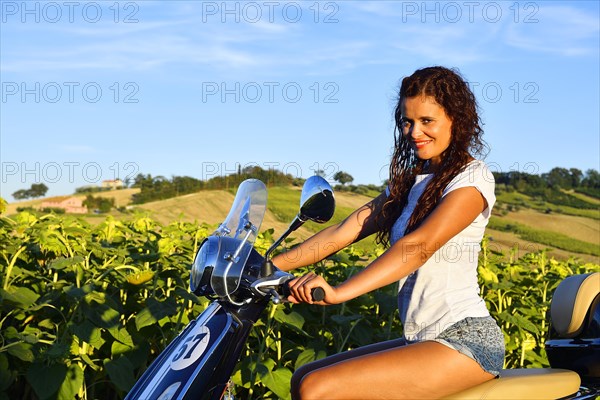 Woman on Vespa Primavera scooter in front of sunflower field