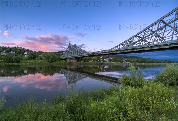 Historical bridge Blaues Wunder is crossing the river Elbe at dust with red cloud above it