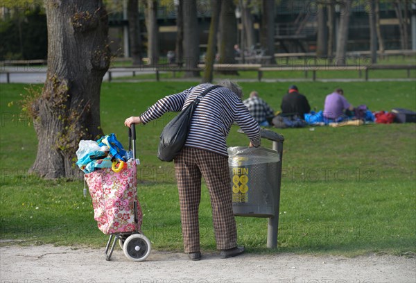 Old woman collects deposit bottles from garbage can