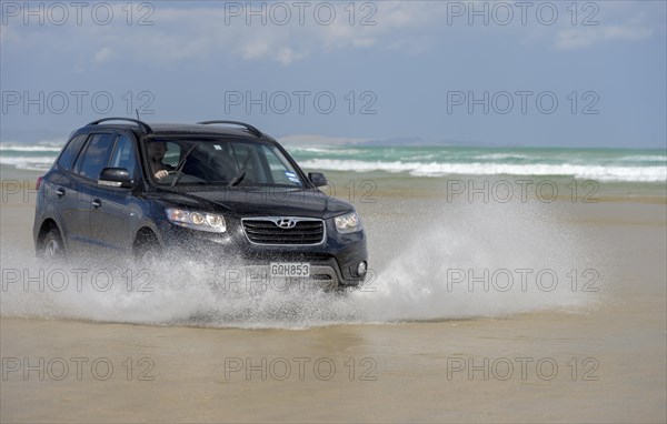 Black Hyundai Santa Fe 4x4 off-road vehicle drives on the sandy beach of Ninety Mile Beach in the water