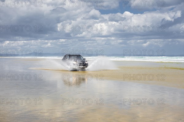 Black Hyundai Santa Fe 4x4 off-road vehicle drives on the sandy beach of Ninety Mile Beach in the water