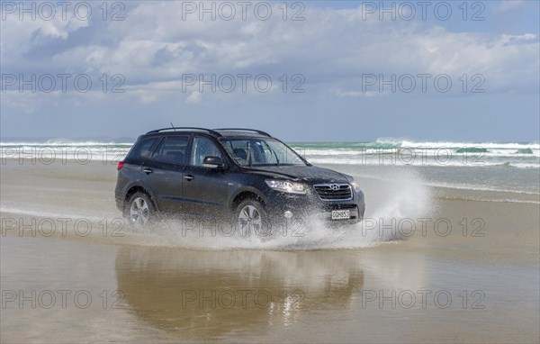 Black Hyundai Santa Fe 4x4 off-road vehicle drives on the sandy beach of Ninety Mile Beach in the water