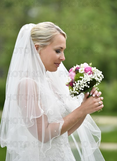 Bride in wedding dress with veil looking at bridal bouqet