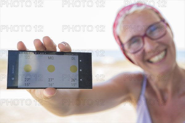 Laughing woman on the beach happy about sunny weather in the weather forecast on her smartphone