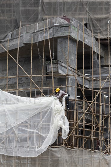 Workers attached a tarpaulin to a scaffolding of bamboo